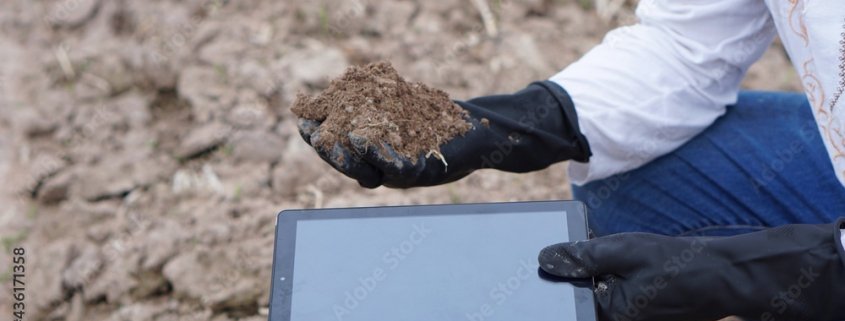 Hands in black gloves hold a smart tablet and soil