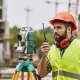 A land surveyor in hard hat and safety vest speaks into a walkie talkie