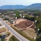 Aerial view of a cleared plot of land outlined with a dashed line and markers. It's beside a road with scattered houses and lush mountains in the background.